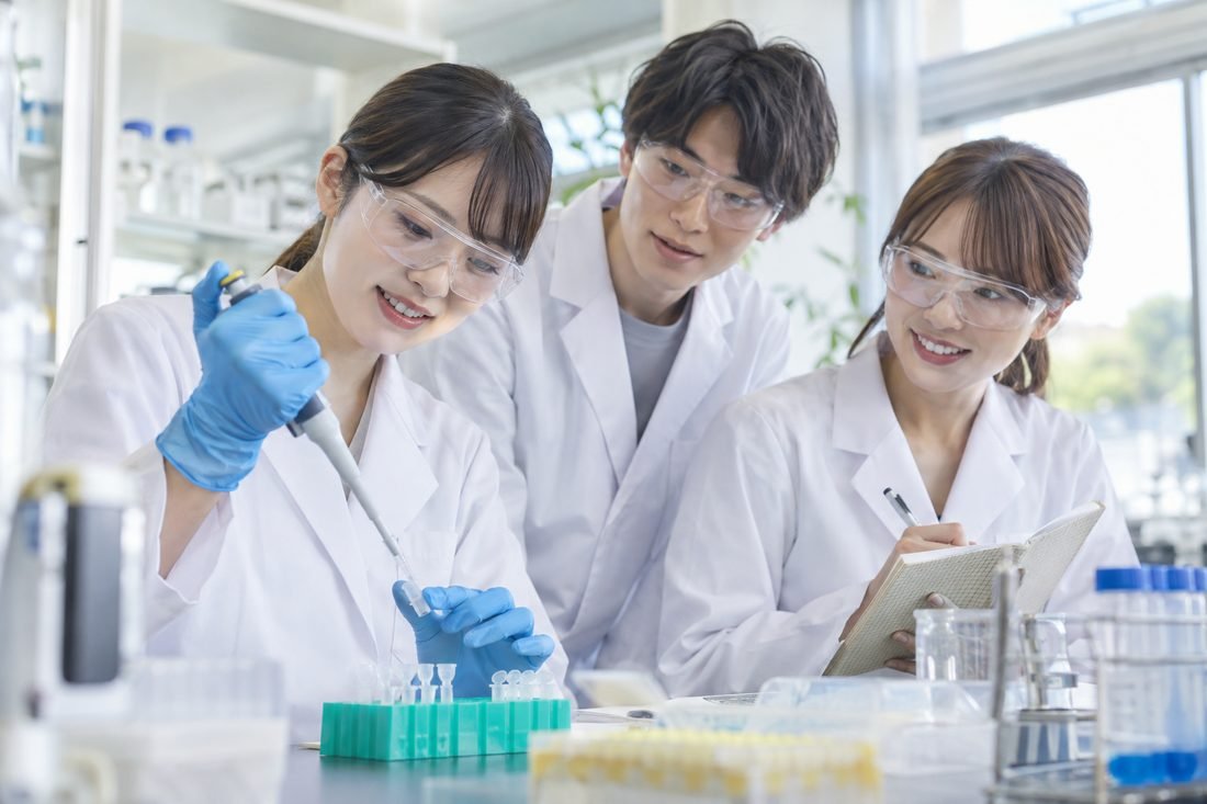 白衣の学生たちが実験を学ぶ様子を描いたイメージ